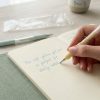 Mano escribiendo en libreta con bolígrafo pastel amarillo