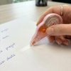 Una mano utiliza un corrector de cinta rosa sobre papel