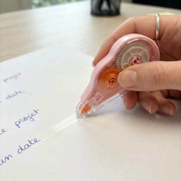 Una mano utiliza un corrector de cinta rosa sobre papel