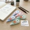 Correctores de cinta en colores pastel junto a un cuaderno y bolígrafos
