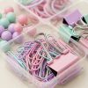 Primer plano de clips y pinzas pastel en su recipiente, con gomas elásticas y chinchetas de cabeza redonda