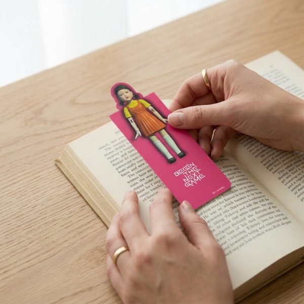 Manos colocando el marcapáginas rosa de Squid Game en un libro.
