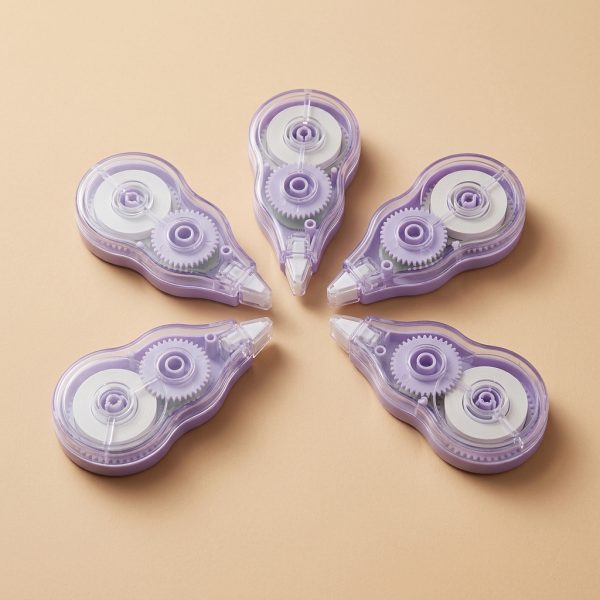 Cinco correctores de cinta lila con carcasa transparente dispuestos sobre un fondo beige