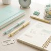 Escritorio con bolígrafos pastel verde menta y amarillo, agenda y material de papelería