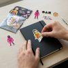 Manos colocando una pegatina de Squid Game sobre un cuaderno