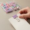 Mano sosteniendo documentos sujetos con una pinza lila, con el set de escritorio al fondo
