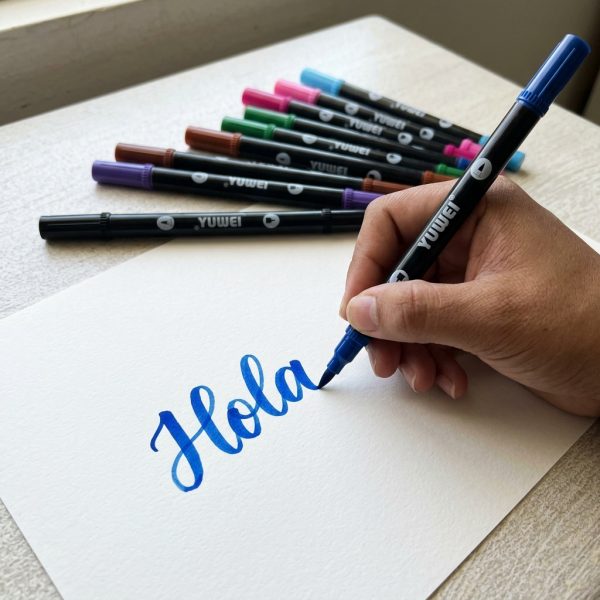Mano escribiendo Hola en azul con un rotulador de punta pincel YUWEI.