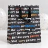 Bolsa negra Happy Birthday sobre mesa blanca con globos al fondo