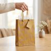 Bolsa de regalo kraft con arcoíris amarillos y asas doradas, en uso con papel de seda decorativo