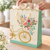 Bolsa de regalo con bicicleta dorada, flores y borde ondulado — en uso