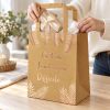 Bolsa de regalo pequeña kraft con hojas rosa dorado y mensaje francés, en uso con regalo